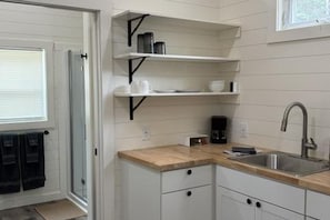 A compact kitchen with white cabinetry, a wooden countertop, a built-in sink, and a window above the sink. - Atlanta South Cabin Getaway, a Cozy Stay Near I-75 (McDonough)