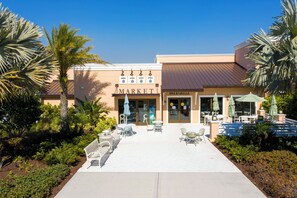 Un bâtiment avec une enseigne indiquant « MARKET », une autre indiquant « BAK & GRILLE », et des tables à l’extérieur, protégées par des parasols.