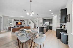 A modern kitchen with a central island, a dining area with a glass table and chairs, and a living room with a sofa and television. - 4BR house with private pool in Solara Resort (Kissimmee)