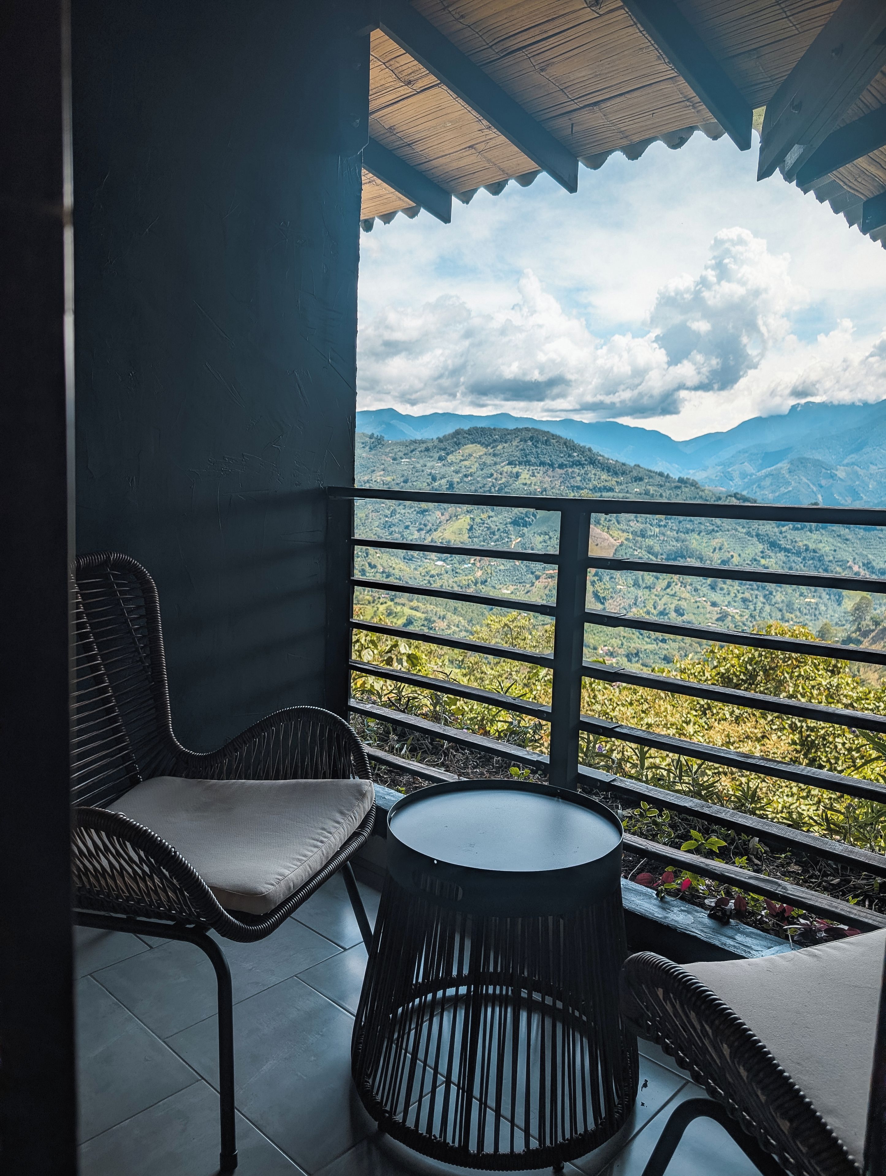 Varanda com vista para uma paisagem montanhosa, com duas cadeiras de vime e uma mesa redonda pequena.