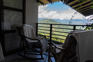 A balcony with a view of green hills and mountains, a rocking chair, and a window with a view of the landscape.