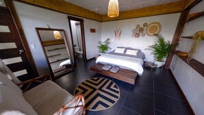 Una habitación con una cama, una silla, una mesita pequeña y una planta en maceta.