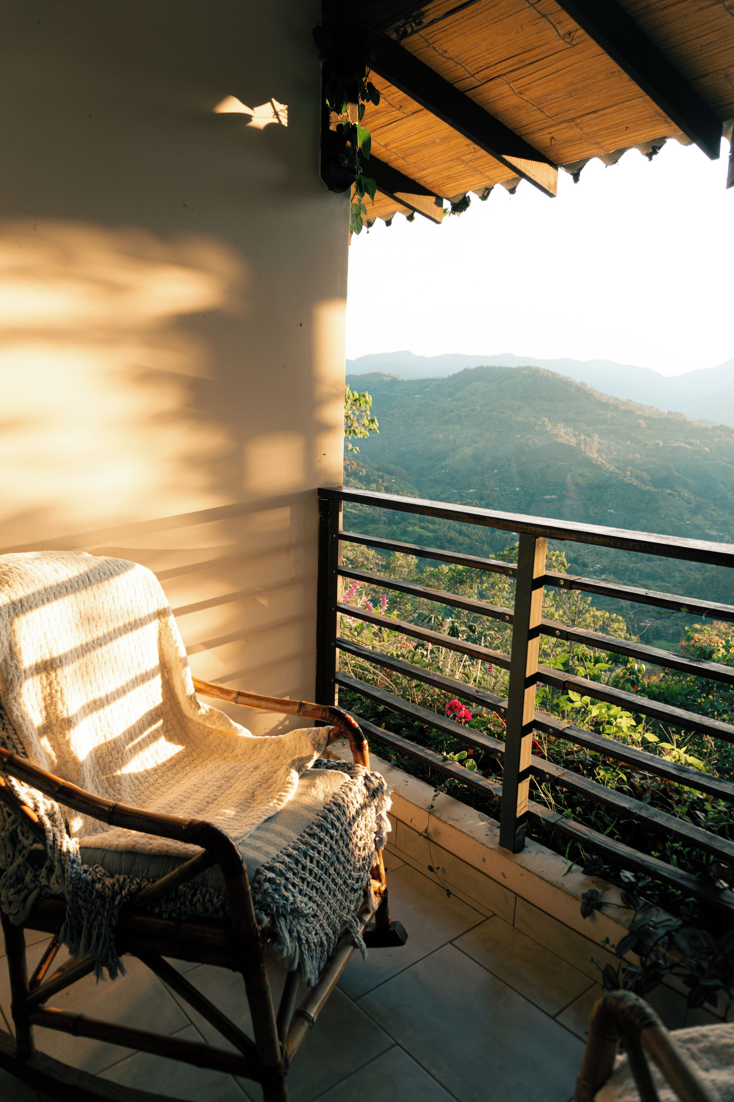 A wicker chair on a balcony with a view of a mountainous landscape.