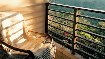 A wicker chair on a balcony with a view of a mountainous landscape.