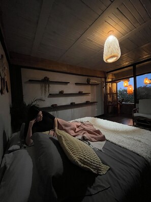 A bedroom with a bed, a hanging light fixture, and a view of the outdoors.