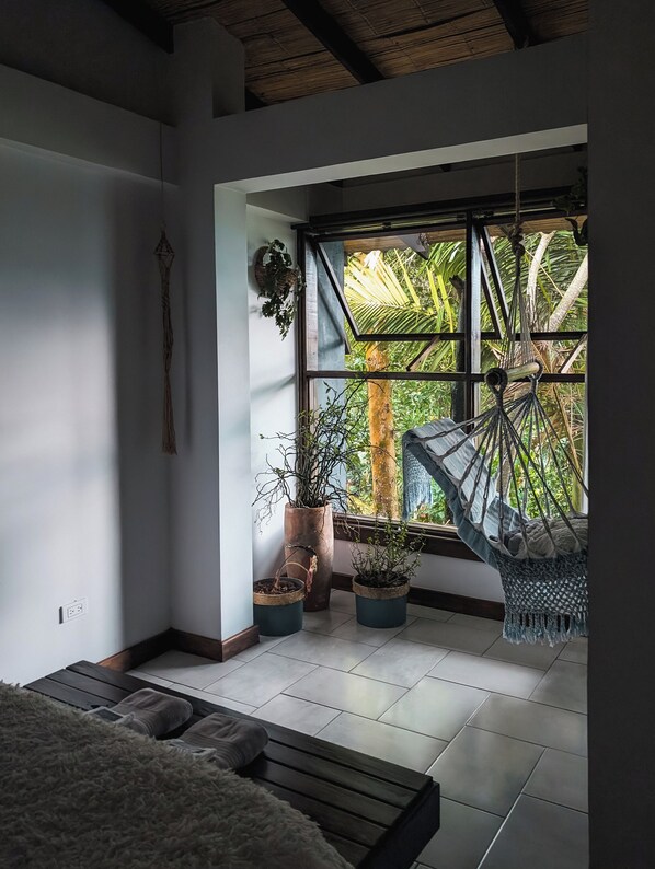 Una habitación con un ventanal grande, una hamaca y varias plantas en macetas.