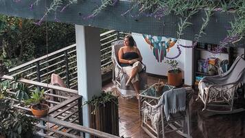 A balcony with a person seated on a chair, surrounded by potted plants and a wooden railing.