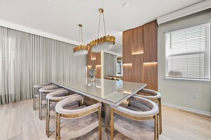 Uma sala de jantar moderna com mesa de vidro, cadeiras estofadas, lustre e um espelho grande.