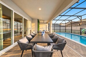 Ein moderner Essbereich im Freien mit Pool, ausgestattet mit einem langen Tisch und Stühlen, einer Glaseinfassung und Blick auf den Pool.