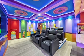 Quarto com parede temática dos Simpsons, porta vermelha e poltronas de couro preto.