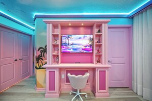 Uma unidade de entretenimento rosa com uma TV de tela plana, prateleiras com figurines e uma cadeira branca na frente.