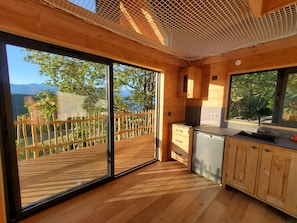 A modern kitchen with a large sliding glass door leading to a deck, wooden cabinets, and a stainless steel sink.