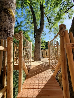 A wooden bridge with rope handrails, surrounded by trees and greenery.