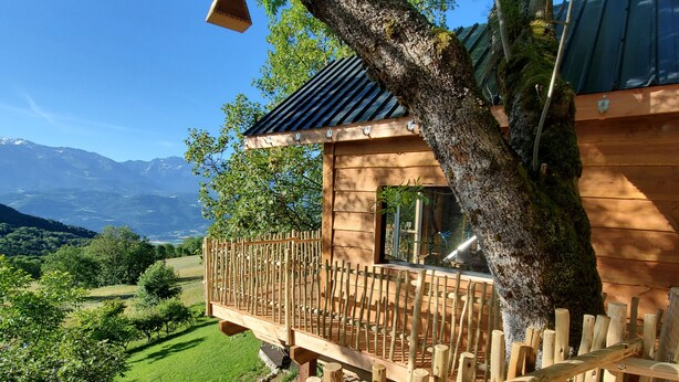 Una terraza de madera con barandilla que da a un paisaje verde exuberante y montañas distantes.