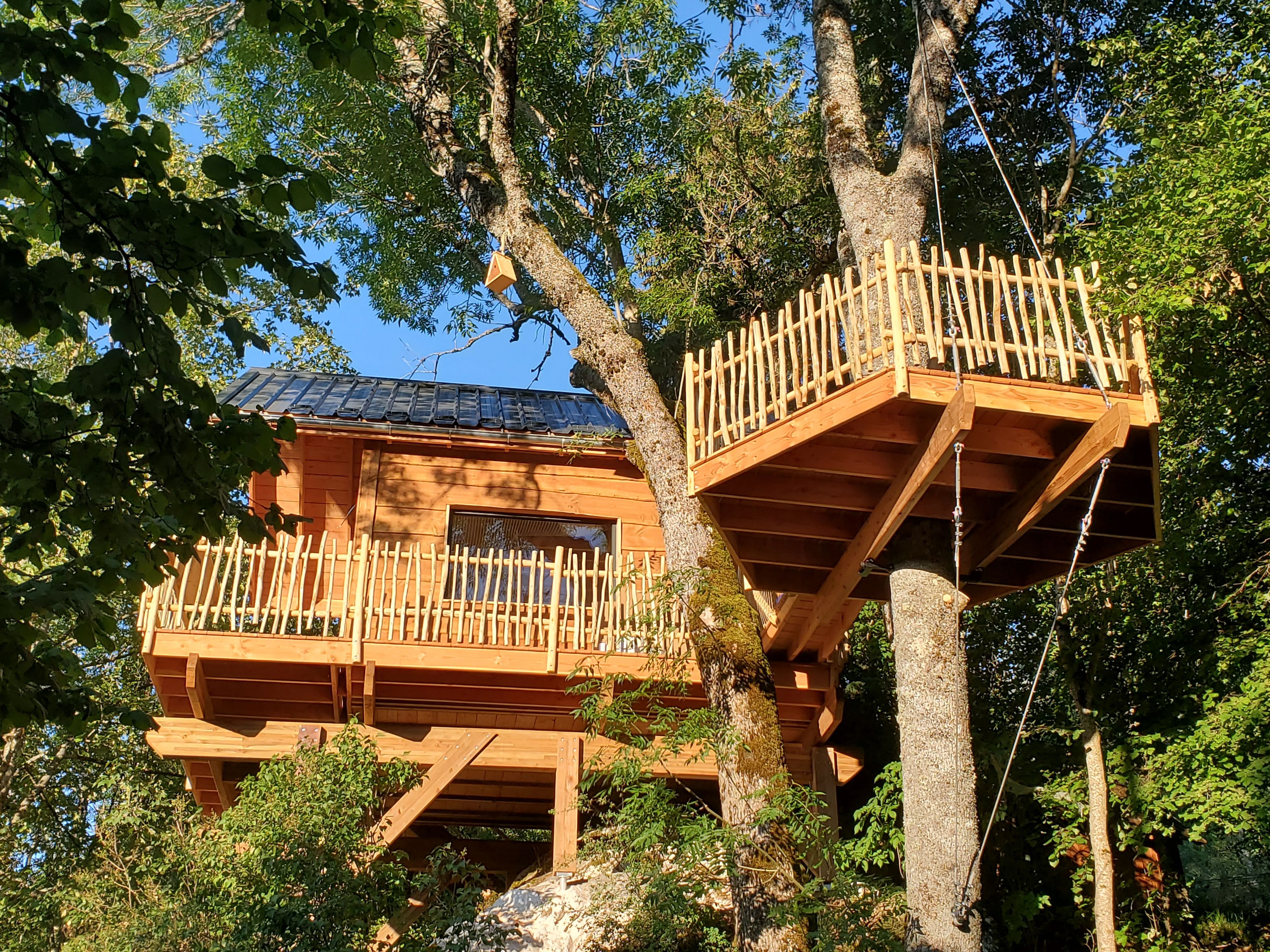 A treehouse with a wooden deck and a window, surrounded by trees.