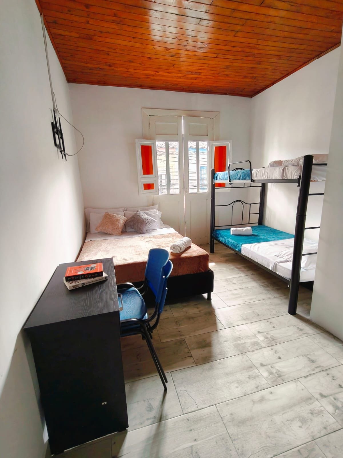 Una habitación pequeña y funcional con una cama individual, un escritorio con silla y una cama litera.