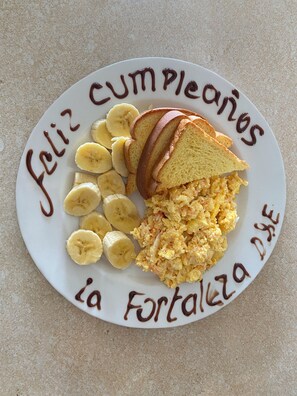 A plate with scrambled eggs, banana slices, and toast, with a birthday message written on it.