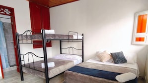 Une chambre avec un lit superposé, un lit simple, un plancher en bois, une porte rouge et un luminaire suspendu.