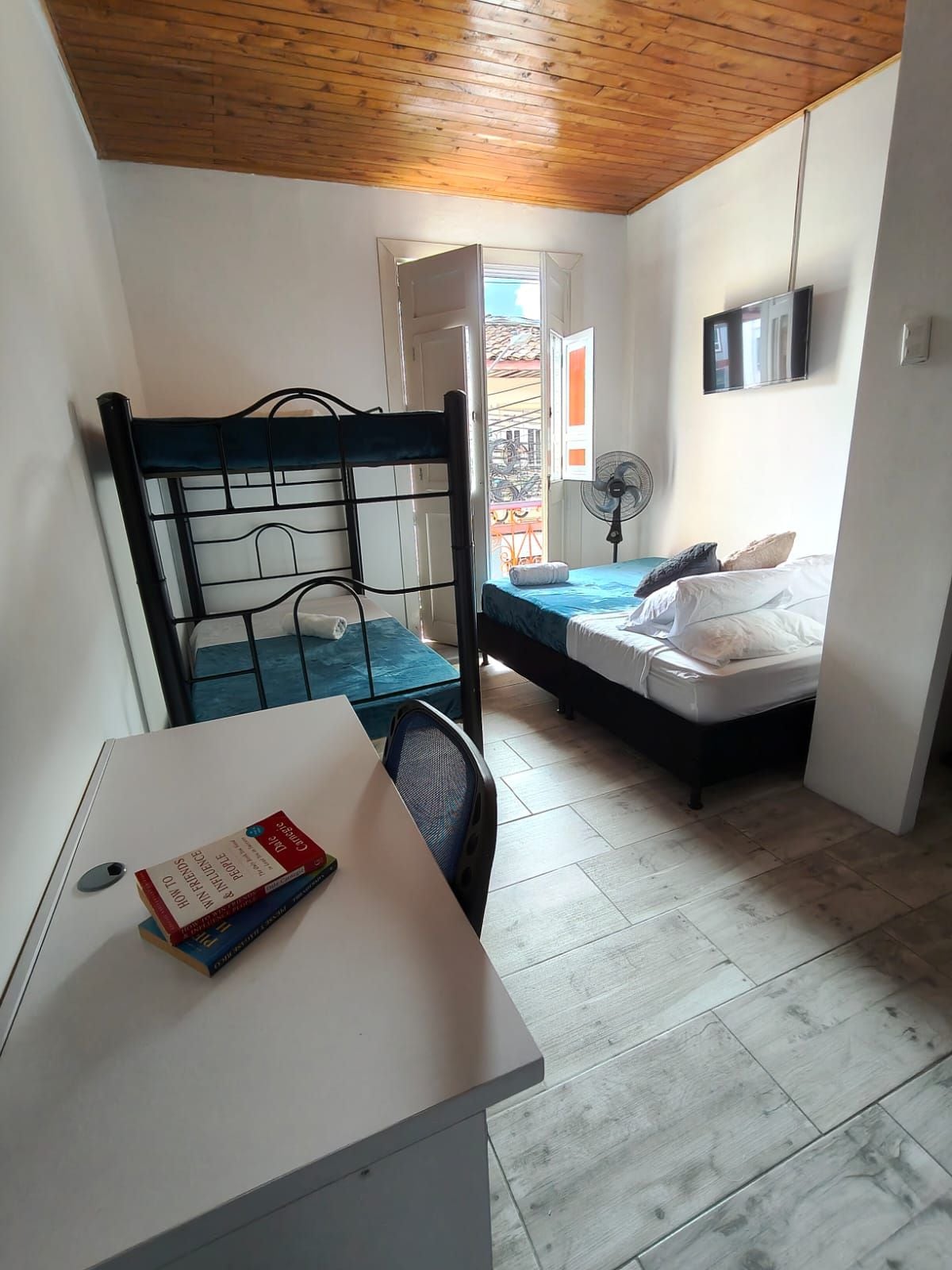 A small, compact room with a single bed, a desk with a chair, and a window with a view of a building.