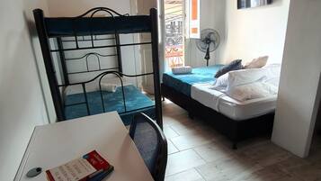 A small, compact room with a single bed, a desk with a chair, and a window with a view of a building.