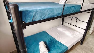 A bunk bed with a blue mattress and white sheets, a rolled towel on the lower bunk, and a wooden floor.