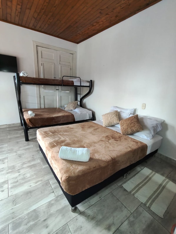A room with two beds, a wooden ceiling, a white door, and a television.