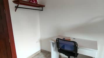 A room with a white desk, a black office chair, a wooden shelf with a decorative item, and a wooden door.