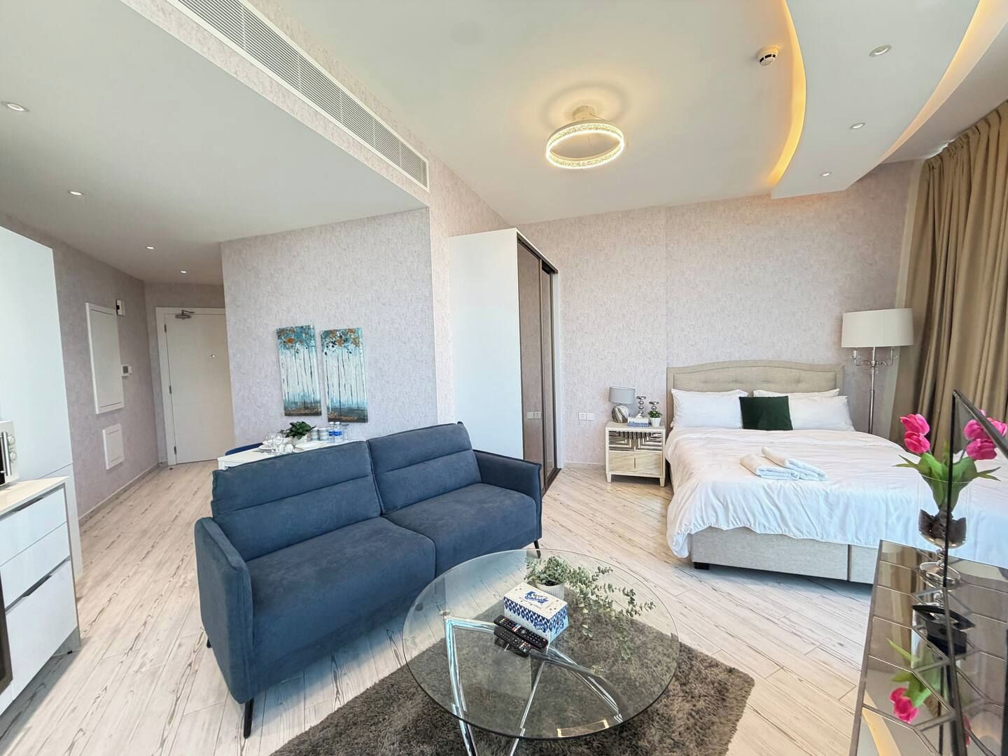 A modern hotel room with a sofa, a glass coffee table, a bed, and a nightstand.