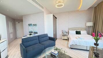 A modern hotel room with a sofa, a glass coffee table, a bed, and a nightstand.