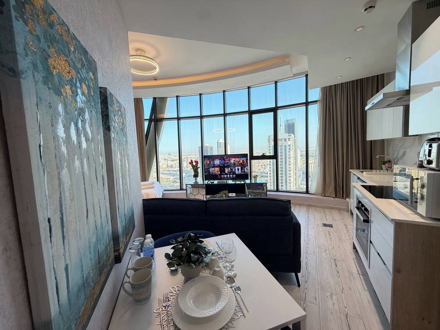 Un soggiorno moderno con zona pranzo, ampie finestre vista città, televisore a schermo piatto e cucina con forno a incasso.