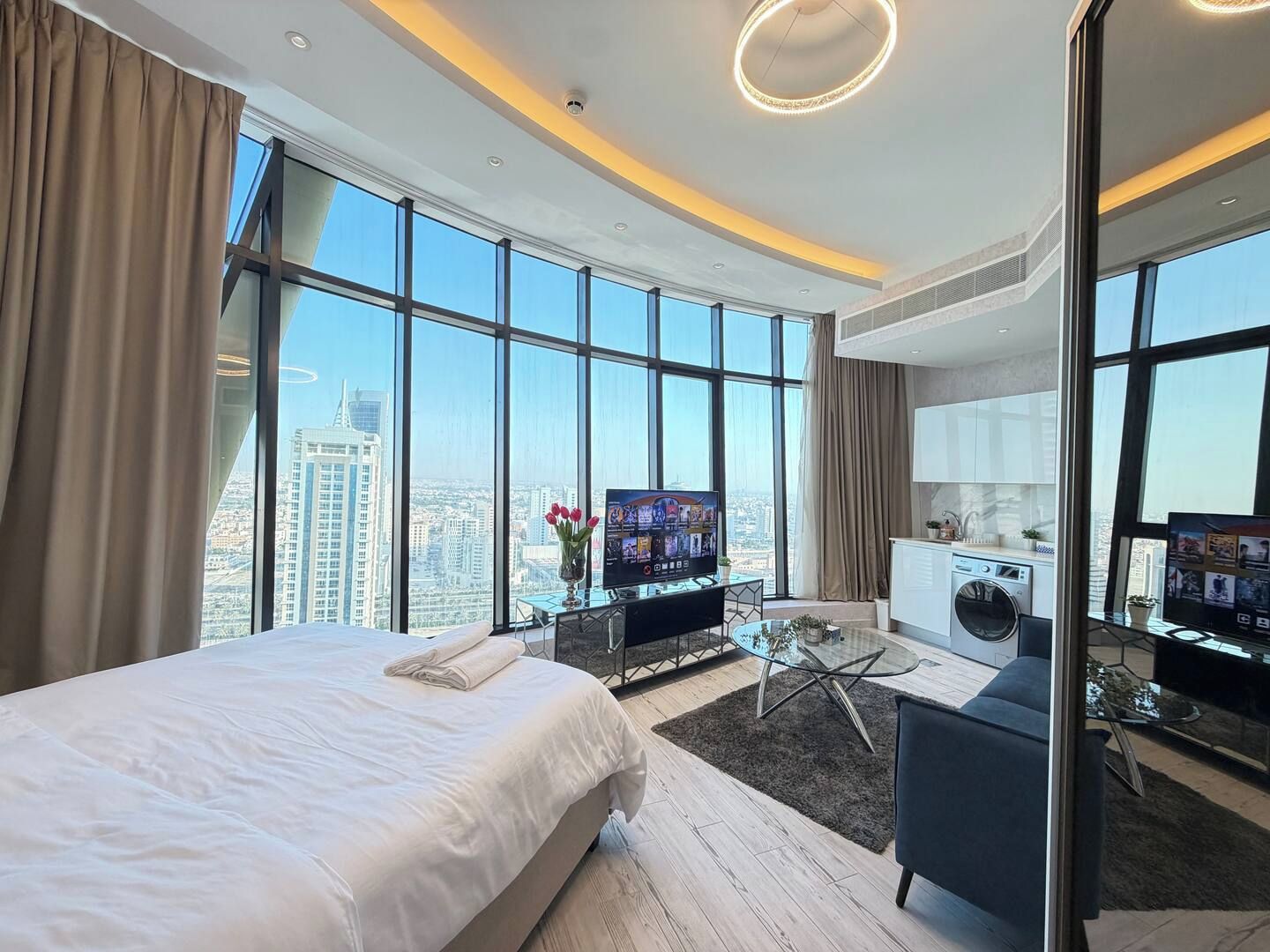 A modern hotel room with a large bed, a desk with a computer, a TV, and a view of the cityscape.