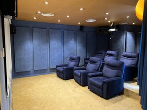 Ein Heimkino mit mehreren dunkelblauen Liegesesseln, einem Teppichboden und einer Decke mit eingelassenen Leuchten.