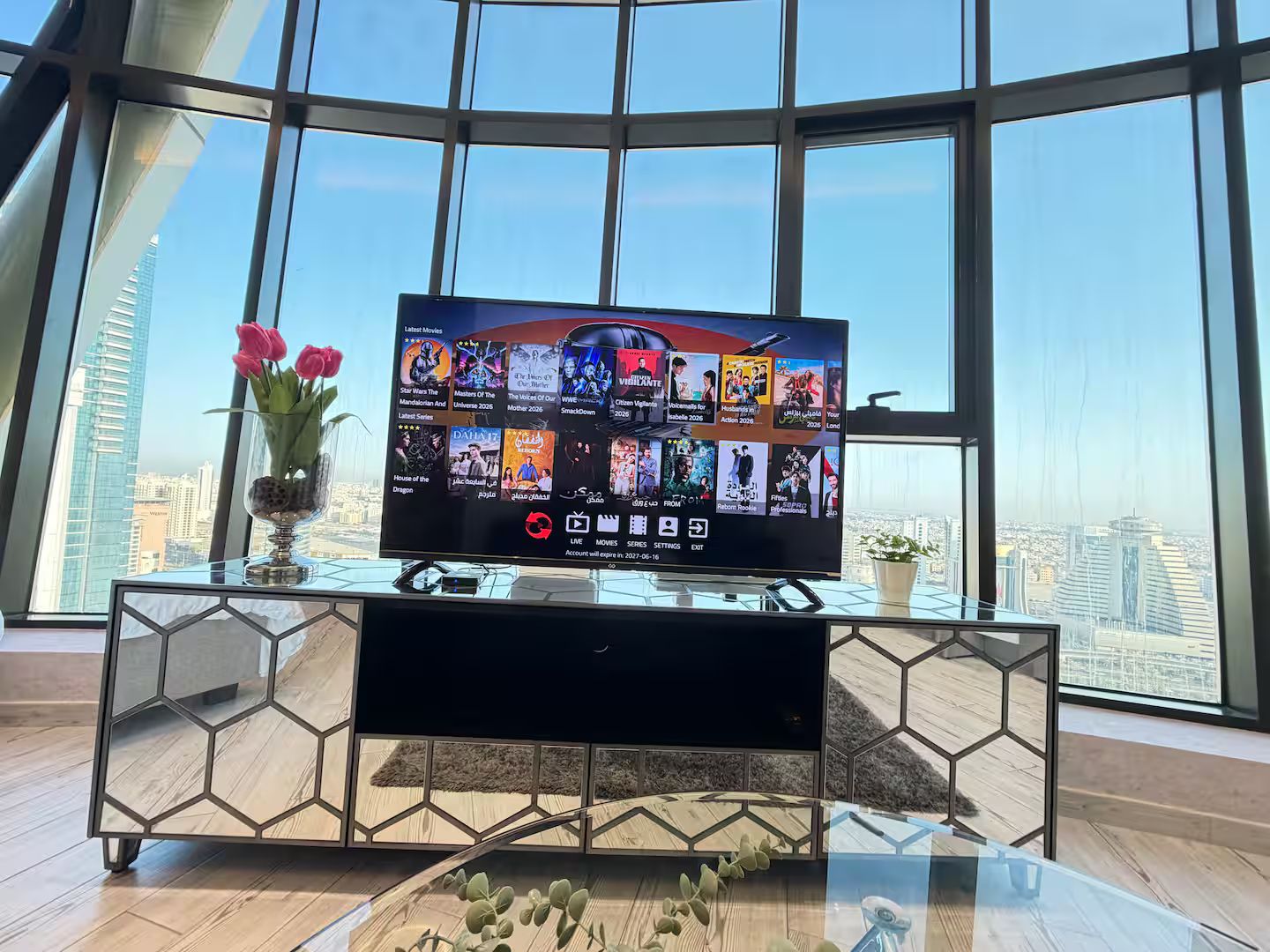A television on a hexagonal console table with a city view.