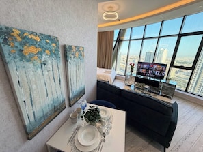 Ein modernes Hotelzimmer mit Essbereich, einer Couch, einem Fernseher und großen Fenstern mit Blick auf die Stadt.