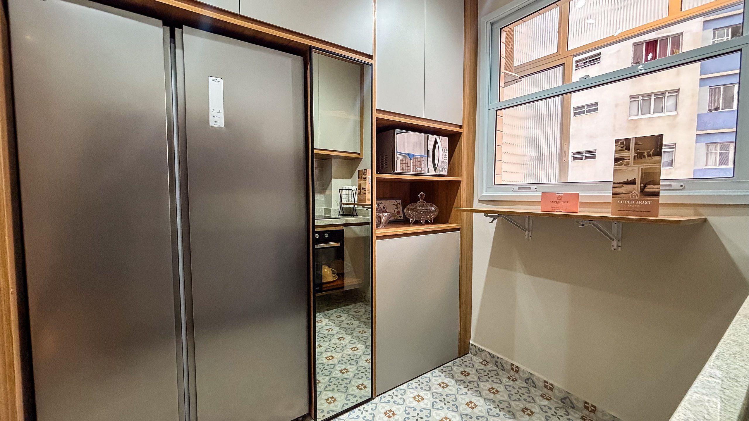 A compact kitchen with a refrigerator, a window with a view of a building, and a shelf with items.