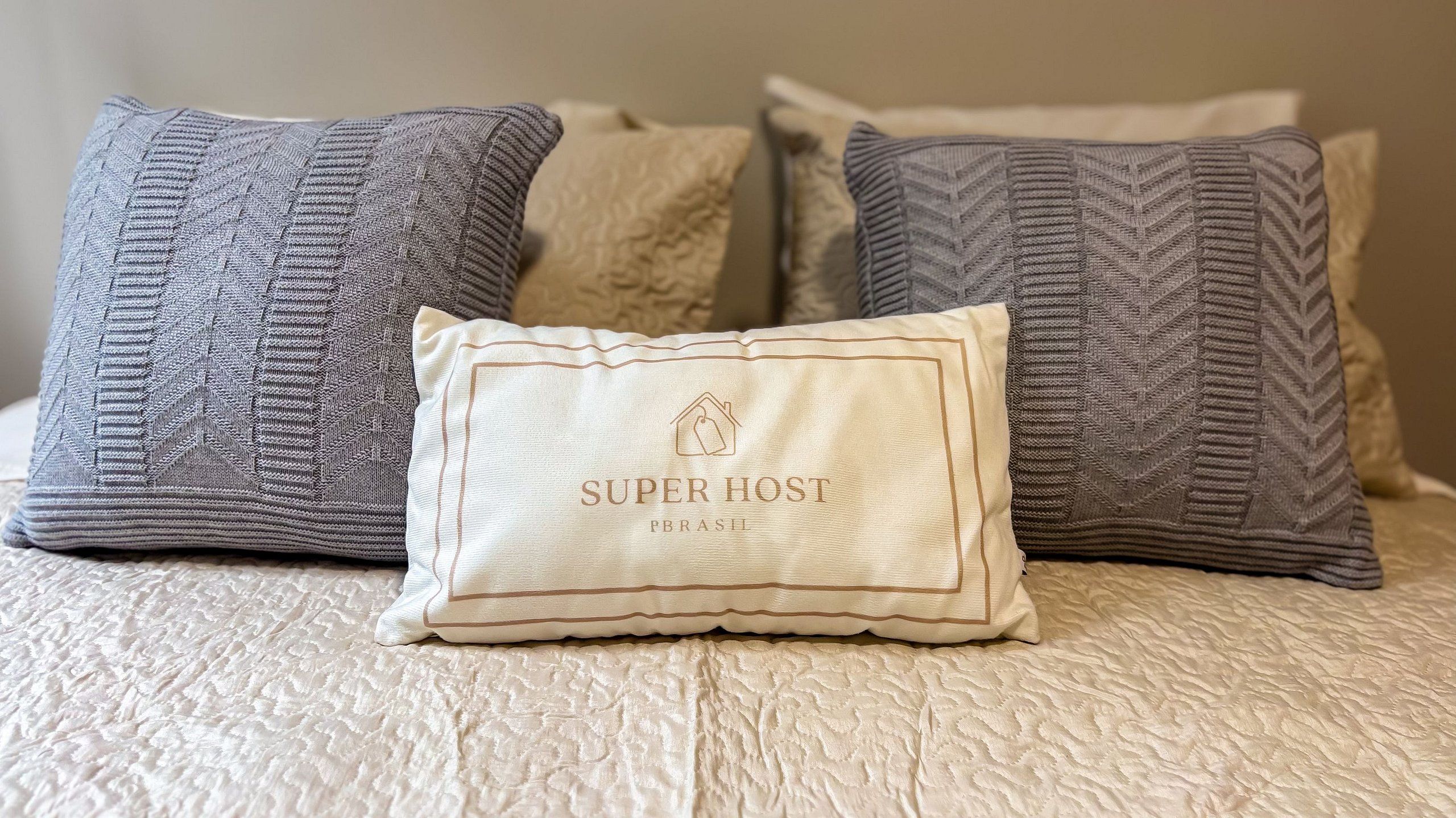 Una cama con una colcha blanca texturizada y tres almohadas con distintos diseños.