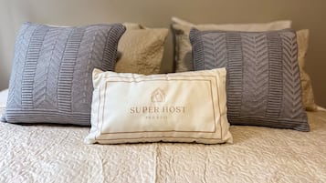 Una cama con una colcha blanca texturizada y tres almohadas con distintos diseños.