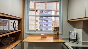 Una habitación con ventana que da a un edificio, una mesa de madera con una caja y estanterías con objetos.