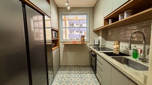 Una cocina compacta con horno integrado, un lavamanos y una ventana con vistas a edificios.