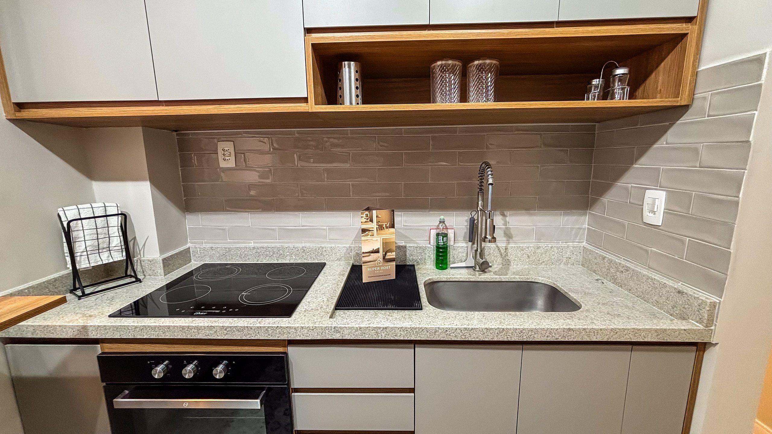 Cocina compacta con cocina por inducción negra, pileta de acero inoxidable y repisa de madera arriba.