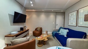 Una sala de estar moderna con un televisor de pantalla plana, un sofá de cuero marrón, un sofá azul, una mesa de centro de madera y una alfombra estampada.
