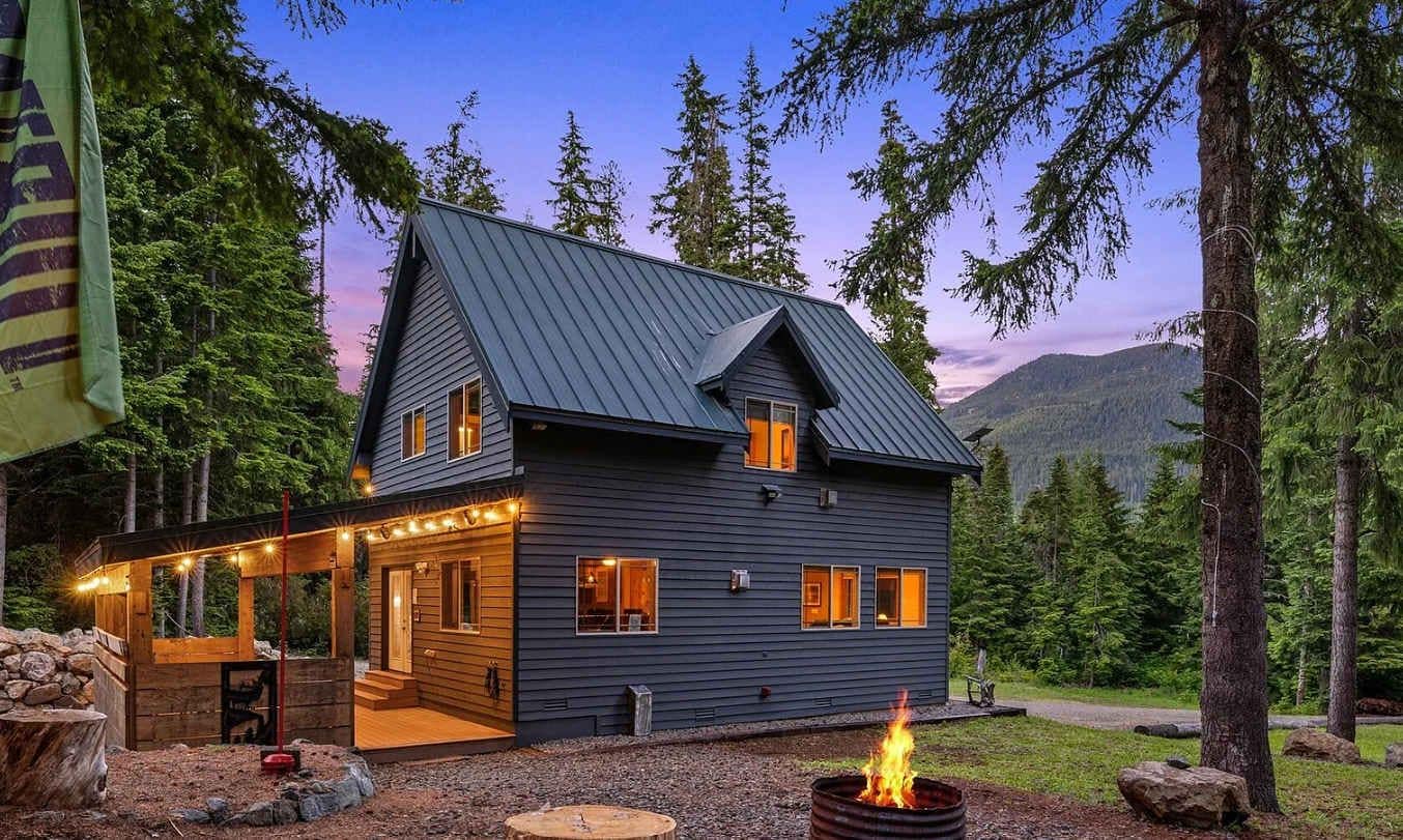 A cabin with a sloped roof, a fire pit, and a porch with string lights.