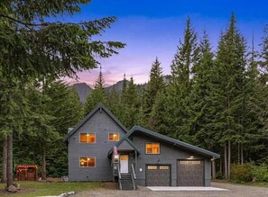 Eine zweistöckige Holzhütte mit Veranda, Garage und Fahnenmast.