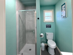 A bathroom with a glass-enclosed shower, a toilet, and a trash bin.