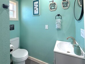 A bathroom with a toilet, sink, and a wall-mounted towel rack. - Pink House in Holiday Island (Eureka Springs)