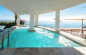 Una piscina amb vista al mar, envoltada de mobiliari exterior i ombrelles.