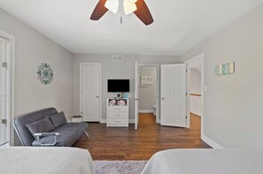 A bedroom with a gray sofa, a TV, and a ceiling fan.