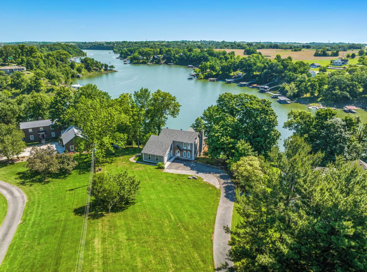 A residential area with a house surrounded by a well-maintained lawn, a driveway, and a river in the background.