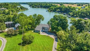 A residential area with a house surrounded by a well-maintained lawn, a driveway, and a river in the background.