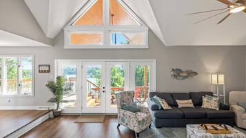 A spacious living room with a high ceiling, a ceiling fan, a large window, and a view of a deck.
